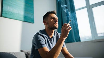 Курение Мужчина сидит с сигаретой на диване